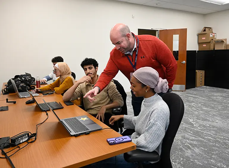 instructor pointing something out to students on computers